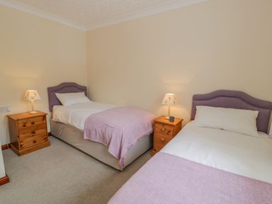 A bedroom with two single beds two wooden nightstands and lamps at Bryn Coch Bach in Dyffryn Ardudwy