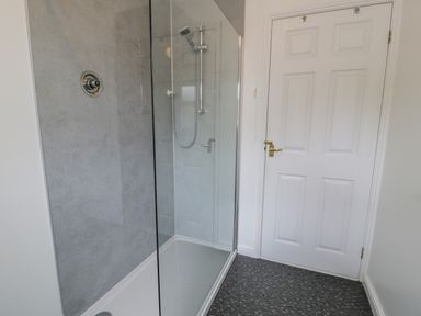 A shower enclosure with glass door and a white paneled door in a bathroom at Bryn Coch Bach in Dyffryn Ardudwy