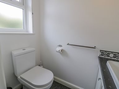 A small bathroom with a toilet next to a frosted window and a sink with counter at Bryn Coch Bach in Dyffryn Ardudwy