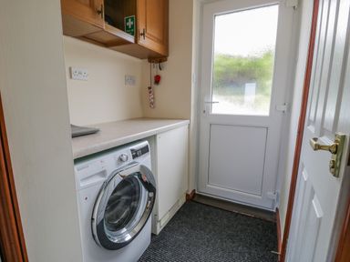 A utility room with a washing machine a countertop wooden cabinets and a white back door at Bryn Coch Bach in Dyffryn Ardudwy
