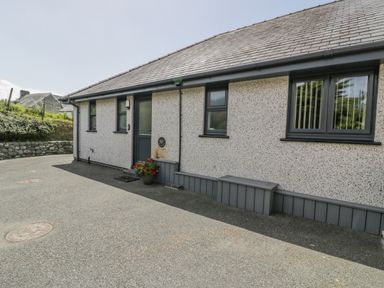 The exterior of a single story house with a speckled wall and dark framed windows and door at Bryn Coch Bach in Dyffryn Ardudwy