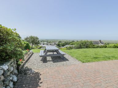 An outdoor area with a picnic table on gravel next to a grass lawn and flowerbed at Bryn Coch Bach in Dyffryn Ardudwy