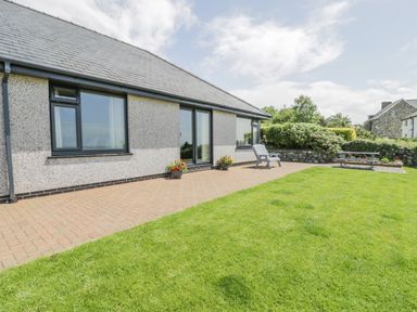 A garden with grass patio chairs and flower pots outside a house at Bryn Coch Bach in Dyffryn Ardudwy