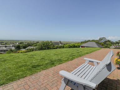 A garden with a paved patio and a bench overlooking a grassy lawn and rooftops at Bryn Coch Bach in Dyffryn Ardudwy