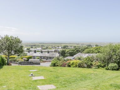 A grassy garden area with trees and shrubs overlooking houses and fields at Bryn Coch Bach in Dyffryn Ardudwy