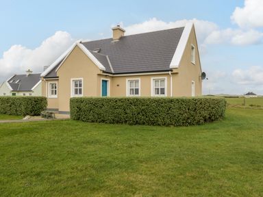 A beige house with gray roof and trimmed hedges in front on a grassy lawn at 8 Lios Na Sioga in Binghamstown near Belmullet County Mayo