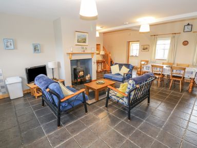 A living room with blue sofas, a wooden coffee table, a wood stove, a dining table with chairs, and a television at 8 Lios Na Sioga in Binghamstown near Belmullet County Mayo