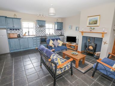 A kitchen and living area with blue cabinets wood stove television and seating at 8 Lios Na Sioga in Binghamstown near Belmullet County Mayo