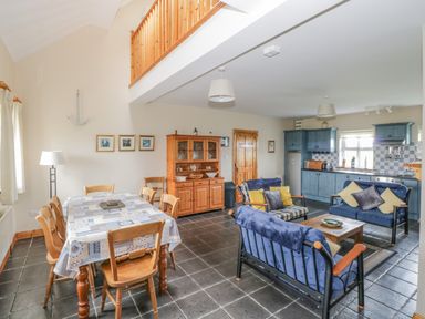 An open plan living room and kitchen with a dining table and wooden chairs a seating area with blue cushioned chairs and sofas blue kitchen cabinets and a wooden display cabinet at 8 Lios Na Sioga in Binghamstown near Belmullet County Mayo