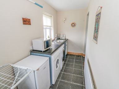 A narrow utility room with a washing machine microwave refrigerator and drying rack at 8 Lios Na Sioga Binghamstown near Belmullet County Mayo