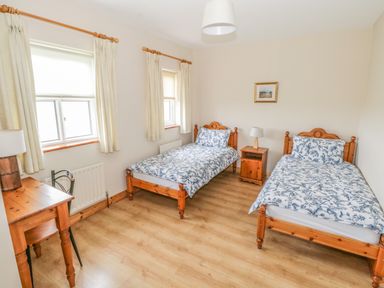 A bedroom with two single beds with floral bedding a wooden desk and chair and two windows at 8 Lios Na Sioga Binghamstown near Belmullet County Mayo
