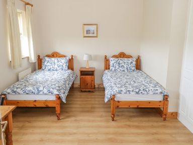 A bedroom with two single wooden beds with floral bedding a wooden nightstand and a lamp at 8 Lios Na Sioga in Binghamstown near Belmullet County Mayo