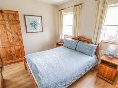 A bedroom with a wooden bed and blue bedding between two windows with curtains at 8 Lios Na Sioga in Binghamstown near Belmullet County Mayo