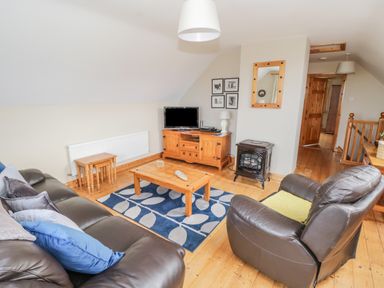 A living room with leather sofas wooden furniture a television and a blue patterned rug at 8 Lios Na Sioga Binghamstown near Belmullet County Mayo