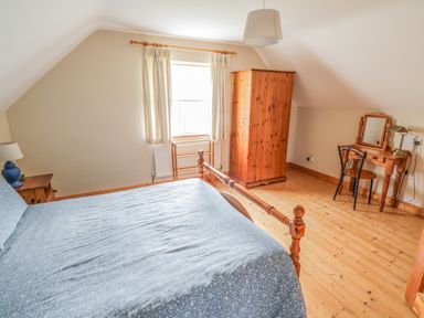 A bedroom with a wooden bed and blue bedspread a wooden wardrobe and a dressing table at 8 Lios Na Sioga Binghamstown near Belmullet County Mayo