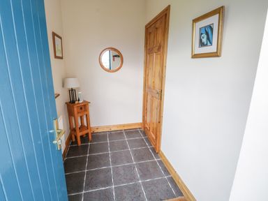 An entryway with a blue door a wooden door a small wooden table with a lamp a round wall mirror and two framed pictures at 8 Lios Na Sioga Binghamstown near Belmullet County Mayo