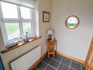 A corner with a window, wooden side table with a lamp, round wall mirror, and boats on the windowsill at 8 Lios Na Sioga Binghamstown near Belmullet County Mayo