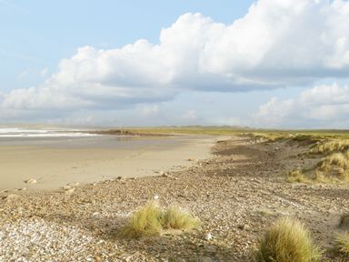 A beach with sand, pebbles, and grassy dunes under a cloudy sky at 8 Lios Na Sioga in Binghamstown near Belmullet County Mayo