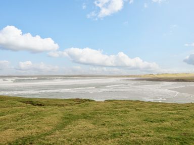 A coastal landscape with green grass in the foreground and waves in the ocean under a partly cloudy sky at 8 Lios Na Sioga Binghamstown near Belmullet County Mayo