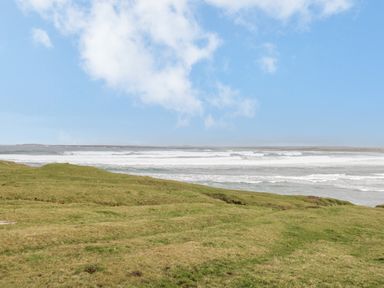 A grassy field near a body of water with waves and a cloudy blue sky at 8 Lios Na Sioga in Binghamstown near Belmullet County Mayo