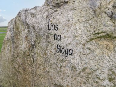 A large rock with the engraved words Lios na Sioga in a grassy outdoor area at 8 Lios Na Sioga in Binghamstown near Belmullet County Mayo