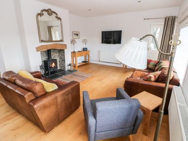 A living room with two brown leather sofas a gray armchair a fireplace a wall mirror a wooden side table and a wall-mounted TV at Llety'r Llwynog in Llanfallteg near Narberth