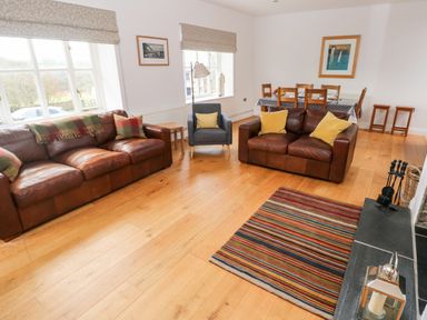 A living room with two brown leather sofas a grey armchair a wooden dining table with chairs and a striped rug at Llety'r Llwynog Llanfallteg near Narberth