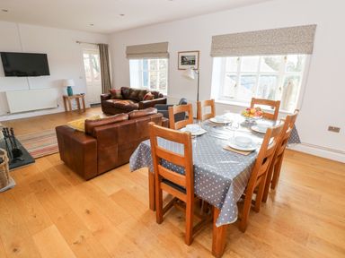 A dining area with a table set for six next to a living space with two brown leather sofas and a wall-mounted TV at Llety'r Llwynog in Llanfallteg near Narberth