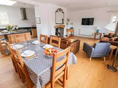 A dining table set with white bowls and glasses next to a living area with brown leather sofas a blue armchair and a wall-mounted TV at Llety'r Llwynog in Llanfallteg near Narberth