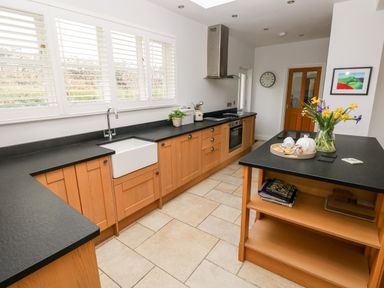 A kitchen with wooden cabinets black countertops a white sink and a wooden island with flowers on a table at Llety'r Llwynog in Llanfallteg near Narberth