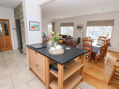 A kitchen island with flowers and tea set and a dining table with chairs near windows in an open plan room at Llety'r Llwynog in Llanfallteg near Narberth