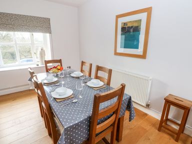 A dining room with a wooden table and six chairs set with white bowls and glasses at Llety'r Llwynog in Llanfallteg near Narberth