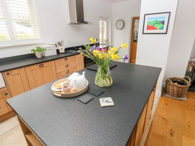 A kitchen with a black countertop island featuring a vase of flowers and a tea set at Llety'r Llwynog in Llanfallteg near Narberth