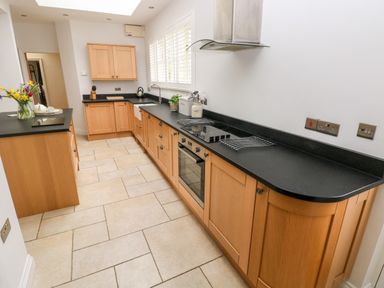 A kitchen with wooden cabinets black countertops and tiled floor at Llety'r Llwynog in Llanfallteg near Narberth