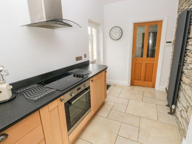 A kitchen with wooden cabinets a black countertop an electric stove an oven a wooden door and a clock on the wall at Llety'r Llwynog in Llanfallteg near Narberth