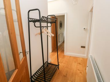 A hallway with wooden floor a black metal clothes rack with wooden hangers a wooden door and a radiator at Llety'r Llwynog in Llanfallteg near Narberth