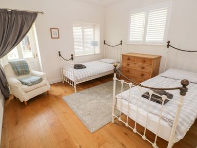 A bedroom with two single beds a wooden dresser an armchair with blankets and curtains at Llety'r Llwynog in Llanfallteg near Narberth