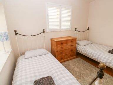 A bedroom with two single beds a wooden chest of drawers and a window with shutters at Llety'r Llwynog in Llanfallteg near Narberth