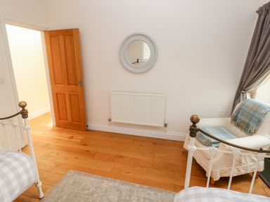 A bedroom with two metal beds a wooden door a round mirror a radiator an armchair with a blanket and curtains at Llety'r Llwynog in Llanfallteg near Narberth