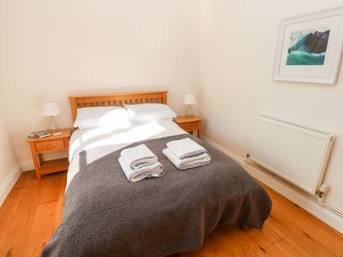A bedroom with a double bed and two folded towels on it two bedside tables with lamps a radiator and a framed picture on the wall at Llety'r Llwynog in Llanfallteg near Narberth