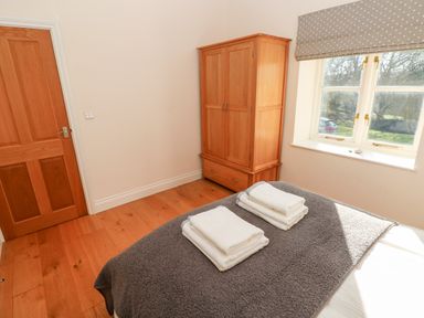 A bedroom with a wooden wardrobe a window with polka dot blinds and towels folded on the bed at Llety'r Llwynog in Llanfallteg near Narberth
