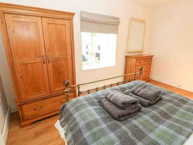 A bedroom with a bed covered with a checkered blanket and folded towels a wooden wardrobe a chest of drawers and a window at Llety'r Llwynog in Llanfallteg near Narberth