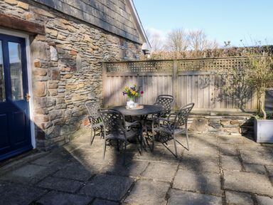 A stone patio with a round metal table and four metal chairs a vase with flowers on the table and a blue door on the left at Llety'r Llwynog in Llanfallteg near Narberth