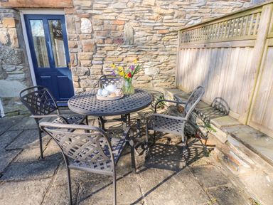 An outdoor patio area with a round metal table and four chairs near a stone wall and a blue door at Llety'r Llwynog in Llanfallteg near Narberth