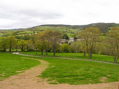 A green field with a dirt path and trees surrounding a village in the distance at Tyn Y Celyn Uchaf in Clocaenog near Ruthin
