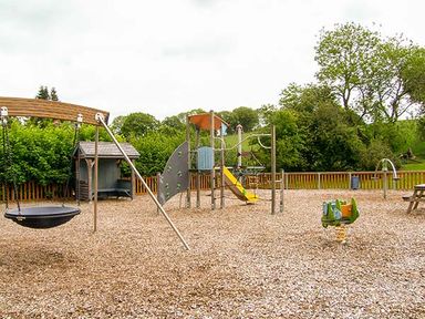 An outdoor playground with a swing, climbing structure with slide, spring rider, and picnic table at Tyn Y Celyn Uchaf in Clocaenog near Ruthin