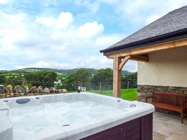 An outdoor hot tub next to a wooden bench with a stone wall and countryside view at Tyn Y Celyn Uchaf in Clocaenog near Ruthin