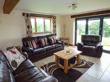 A living room with leather sofas a wooden coffee table and large windows at Tyn Y Celyn Uchaf Clocaenog near Ruthin