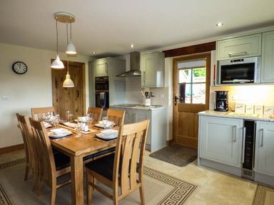 A kitchen and dining area with a wooden dining table set for six near a wooden door and kitchen cabinets at Tyn Y Celyn Uchaf Clocaenog near Ruthin
