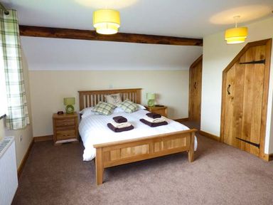 A bedroom with a wooden bed frame two bedside tables lamps and wooden doors at Tyn Y Celyn Uchaf in Clocaenog near Ruthin